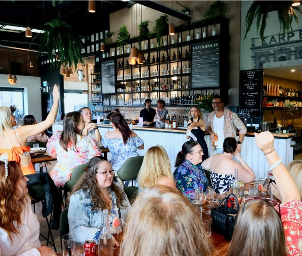 A crowded bar raising glasses while Brydie hosts